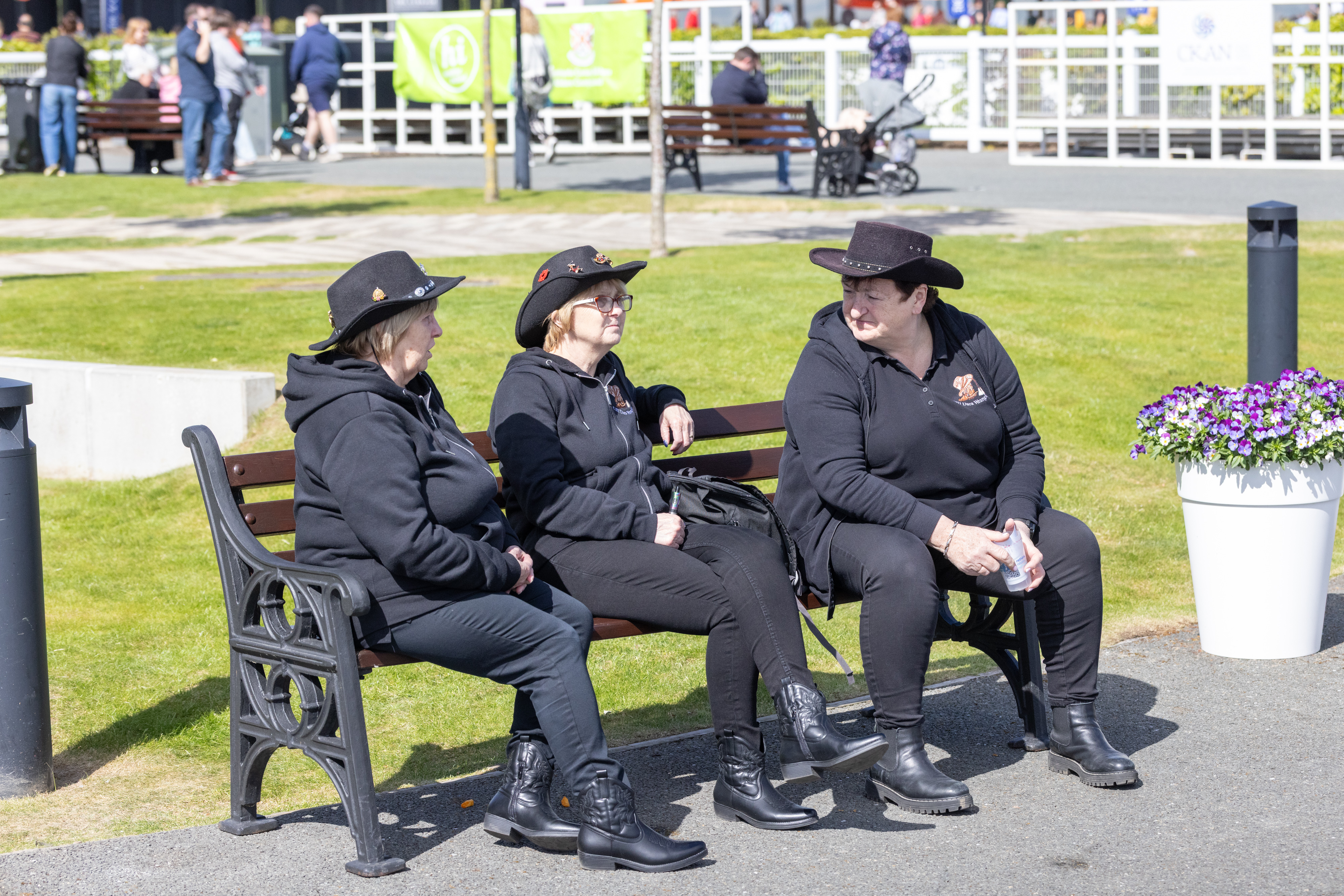 Three people sat on park bench talking. 